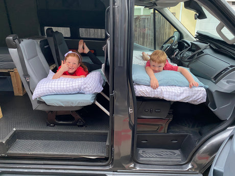 Happy kids relax on beds in an RV rental camper van. Great for family road trips & adventures!