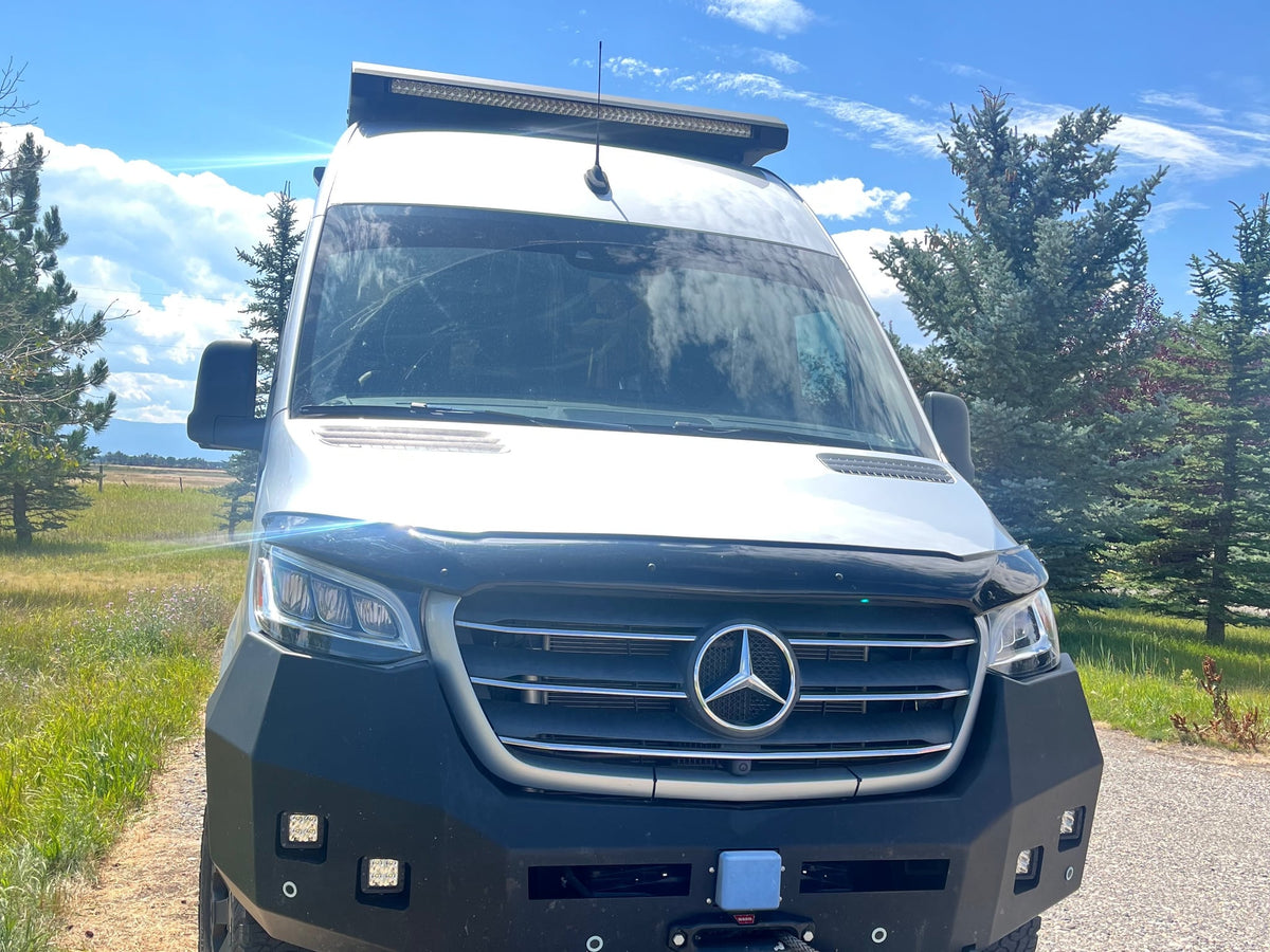  with a ladder & roof rack. Mountains and a tree frame the scenic view.|Silver Mercedes Sprinter RV rental with custom off-road bumper & roof light bar — photo 2