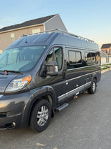 Dark grey Winnebago camper van, perfect for rv rental getaways, parked on a quiet residential street in soft evening light.