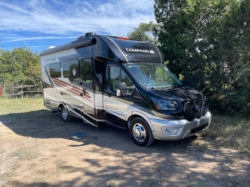 Experience freedom with a Thor Compass AWD rv rental. This black and silver motorhome is parked on a dirt patch outdoors. — photo 2