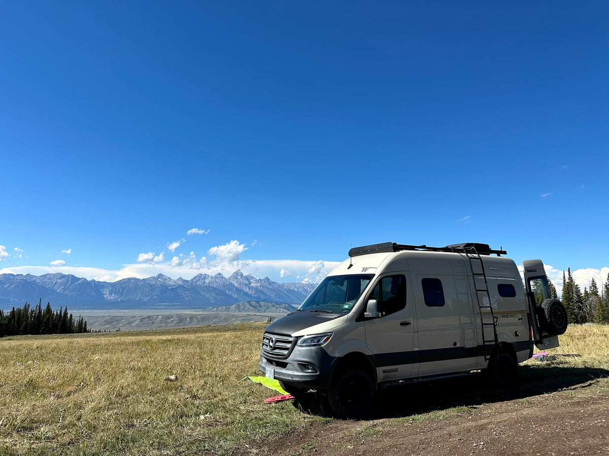  and an orange playpen on shore at sunset.|Winnebago Revel rv rental camper van parked in a scenic mountain landscape with grassy fields under a bright blue sky.|RV rental on a rugged dirt road — photo 4