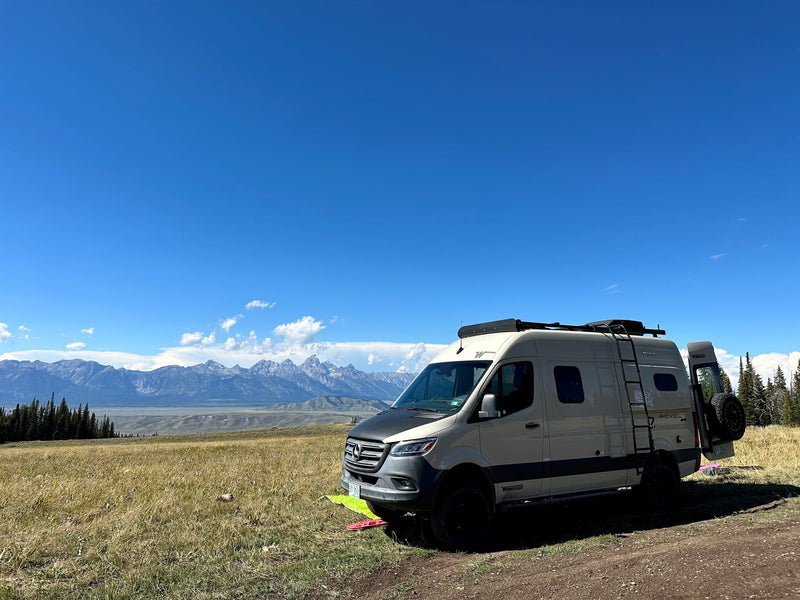  and an orange playpen on shore at sunset.|Winnebago Revel rv rental camper van parked in a scenic mountain landscape with grassy fields under a bright blue sky.|RV rental on a rugged dirt road — photo 4