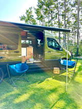 Green adventure RV rental parked on grass with awning extended, blue chairs, and a Yeti cooler. Perfect for outdoor relaxation.