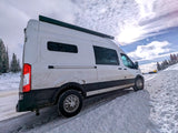 Explore winter wonderland in this rugged white RV rental camper van on a snowy mountain road.