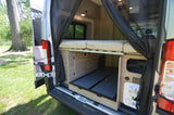 Open back of an RV rental reveals a bed, storage, utility panel, and black mesh curtain inside.