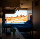 Wake up to amazing views! An RV rental offers a bed, coffee, and a panorama of desert rock formations from its open back.