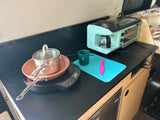Compact RV rental kitchen setup: portable cooktop, pan, pot, coffee maker/toaster oven, mug, and cutting board for easy meals.