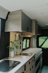 Modern RV rental interior: compact kitchen with sink & cooktop, overhead storage, and bed area for travel comfort.