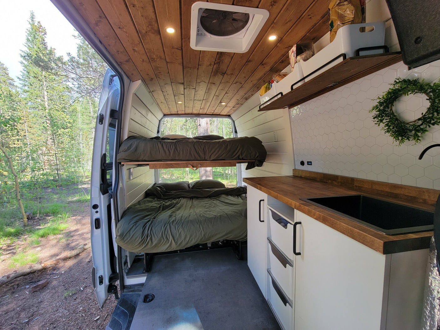 This custom RV rental features cozy bunk beds, a compact kitchen, and woodland views, perfect for an adventure.
