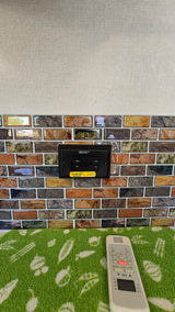 RV rental: GFCI inverted solar outlet on stone-look tile backsplash. An AC remote on a green mat provides comfort control.