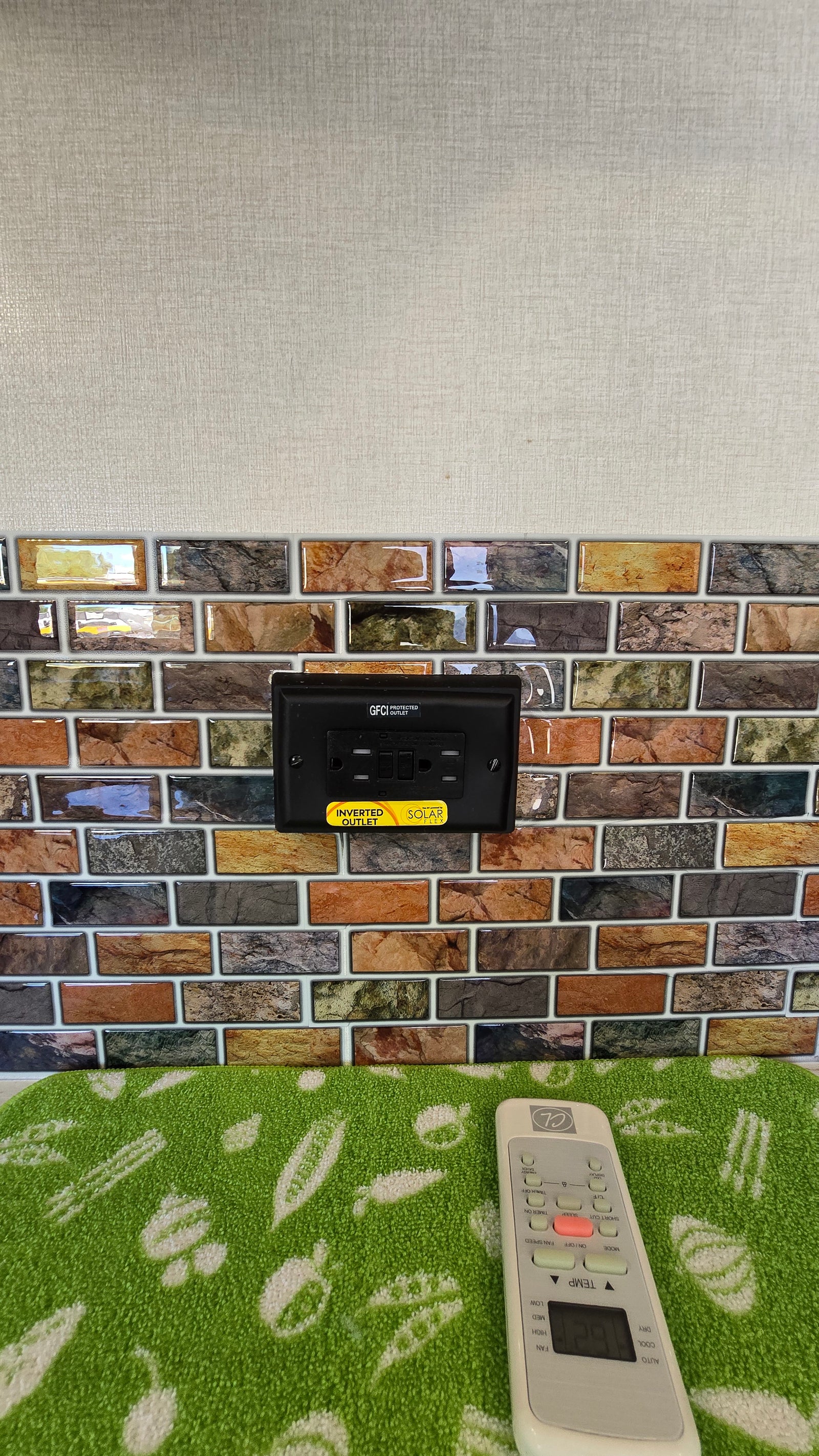 RV rental: GFCI inverted solar outlet on stone-look tile backsplash. An AC remote on a green mat provides comfort control.