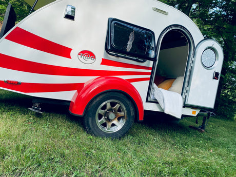A vibrant red-striped T@G teardrop camper RV rental sits on green grass, inviting outdoor adventures.