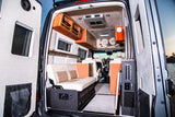 Modern RV rental interior from rear: custom seating, orange accents, storage, and control panels. Spacious mobile living space.