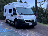 White Winnebago Ram ProMaster camper van, possibly an RV rental, parked on a colorful chalk-covered road.