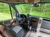 Driver's view from an rv rental: a detailed look at the van's cockpit, dashboard, and vibrant forest outside.