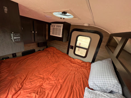 This rv rental shows a cozy bedroom with an orange bed, AC unit, thermostat, and storage, perfect for your next trip.