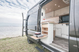 Experience outdoor cooking with this RV rental camper van's pull-out kitchen, parked by a bay with a distant bridge.