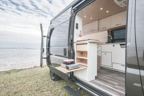 Experience outdoor cooking with this RV rental camper van's pull-out kitchen, parked by a bay with a distant bridge.