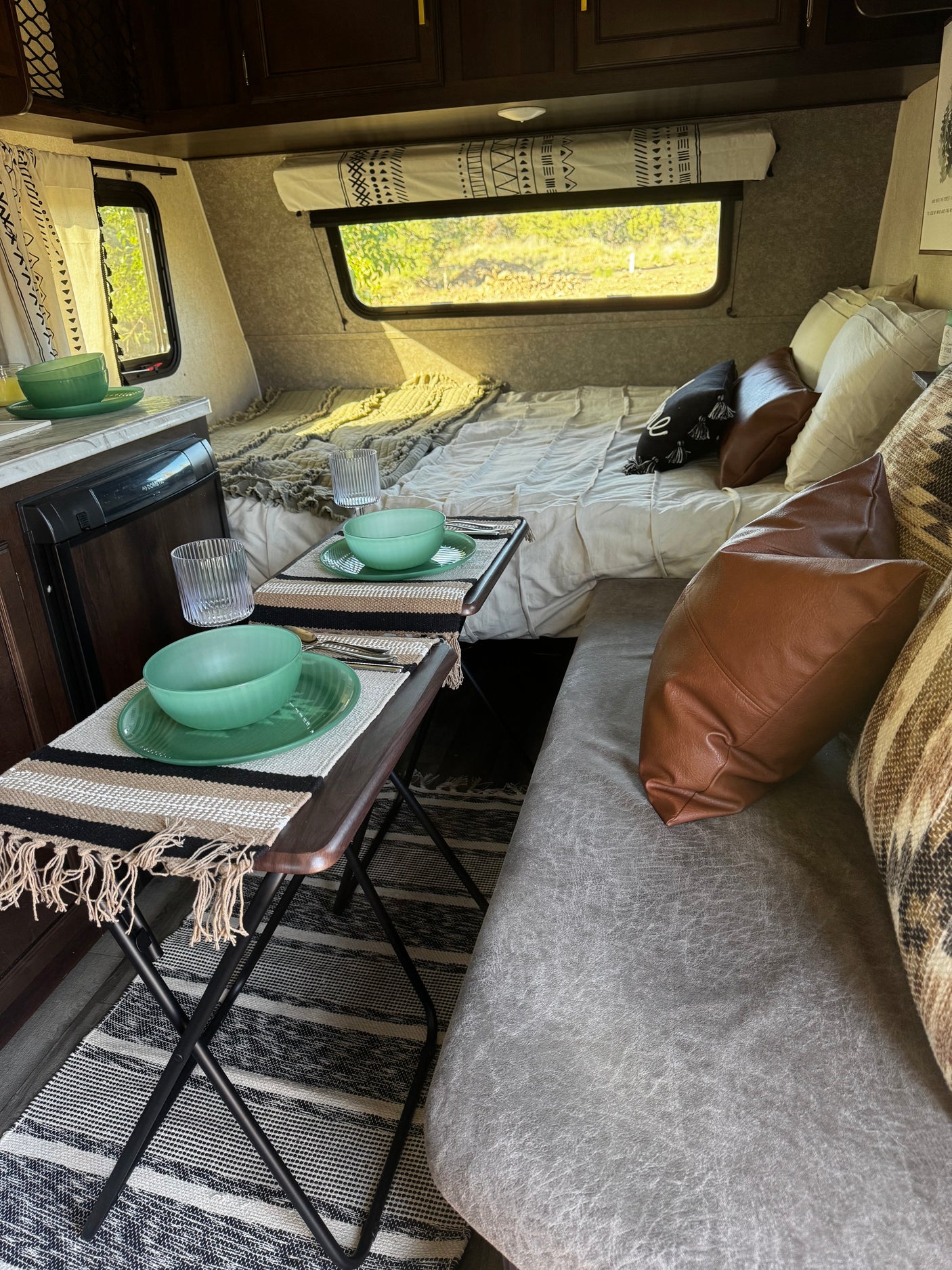 Cozy rv rental interior: A full bed, twin dining tables with settings, and a comfortable sofa are visible.