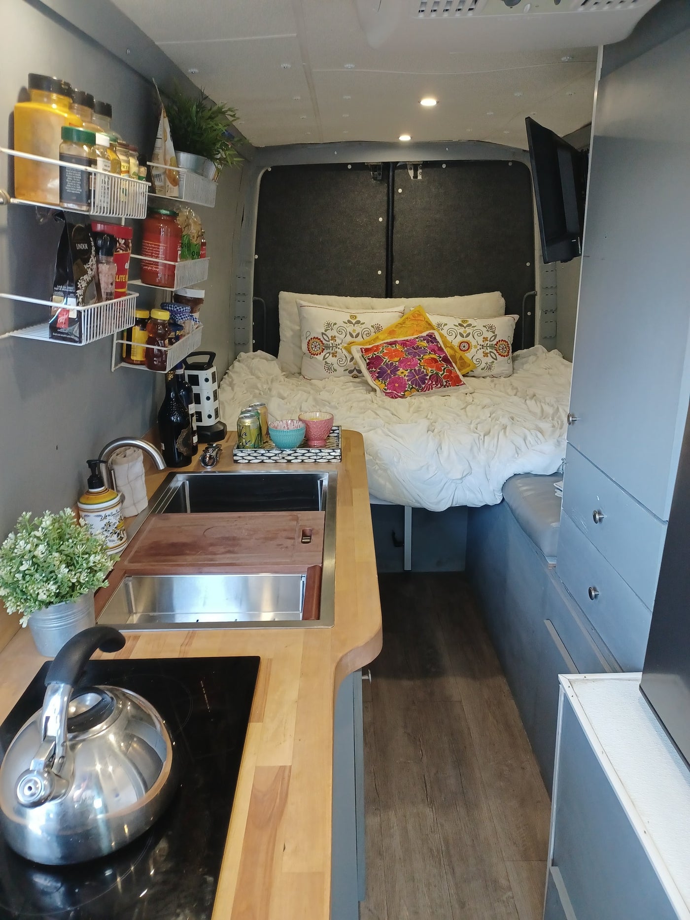 Explore this RV rental's inviting interior: cozy bed, modern kitchen with induction stove, and smart storage solutions. — photo 11