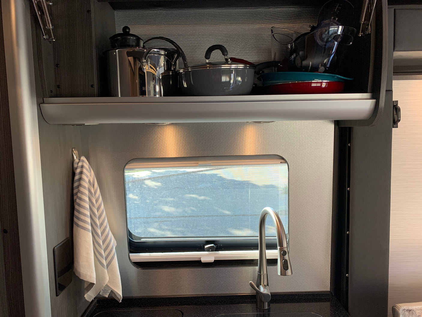 Efficient RV rental galley: overhead cabinets with pots, pans, a sink with pull-down faucet, and window view.