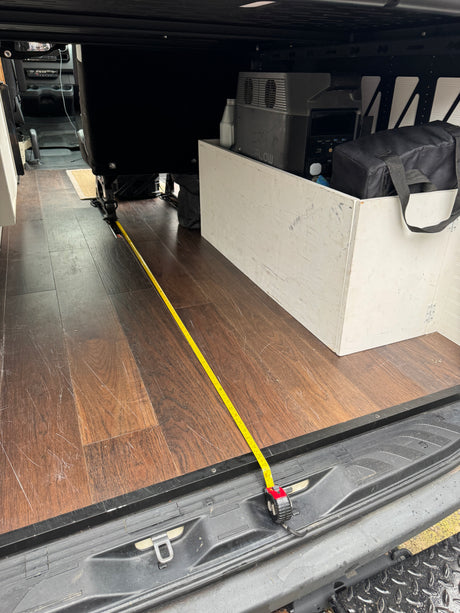 Inside an RV rental: a measuring tape spans the wood floor from the back door to a seat. Portable power station visible.