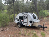 A compact RV rental teardrop trailer parked in a serene forest setting, perfect for outdoor camping trips.