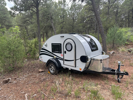 A compact RV rental teardrop trailer parked in a serene forest setting, perfect for outdoor camping trips.