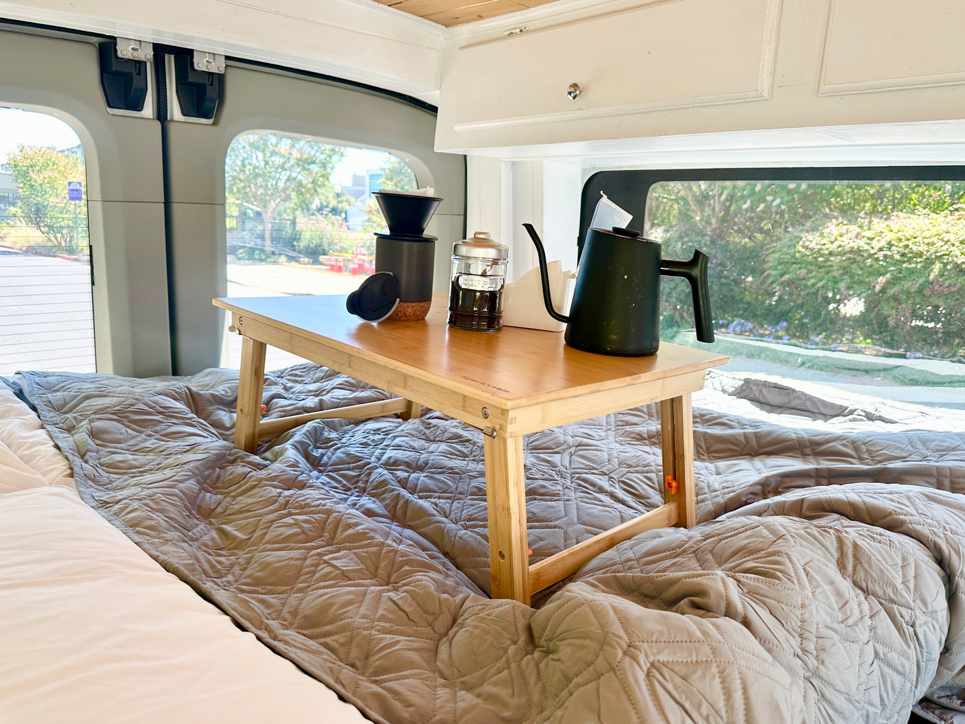 Morning coffee in your RV rental, served on a cozy bed with a wooden tray holding a pour-over kit and kettle.