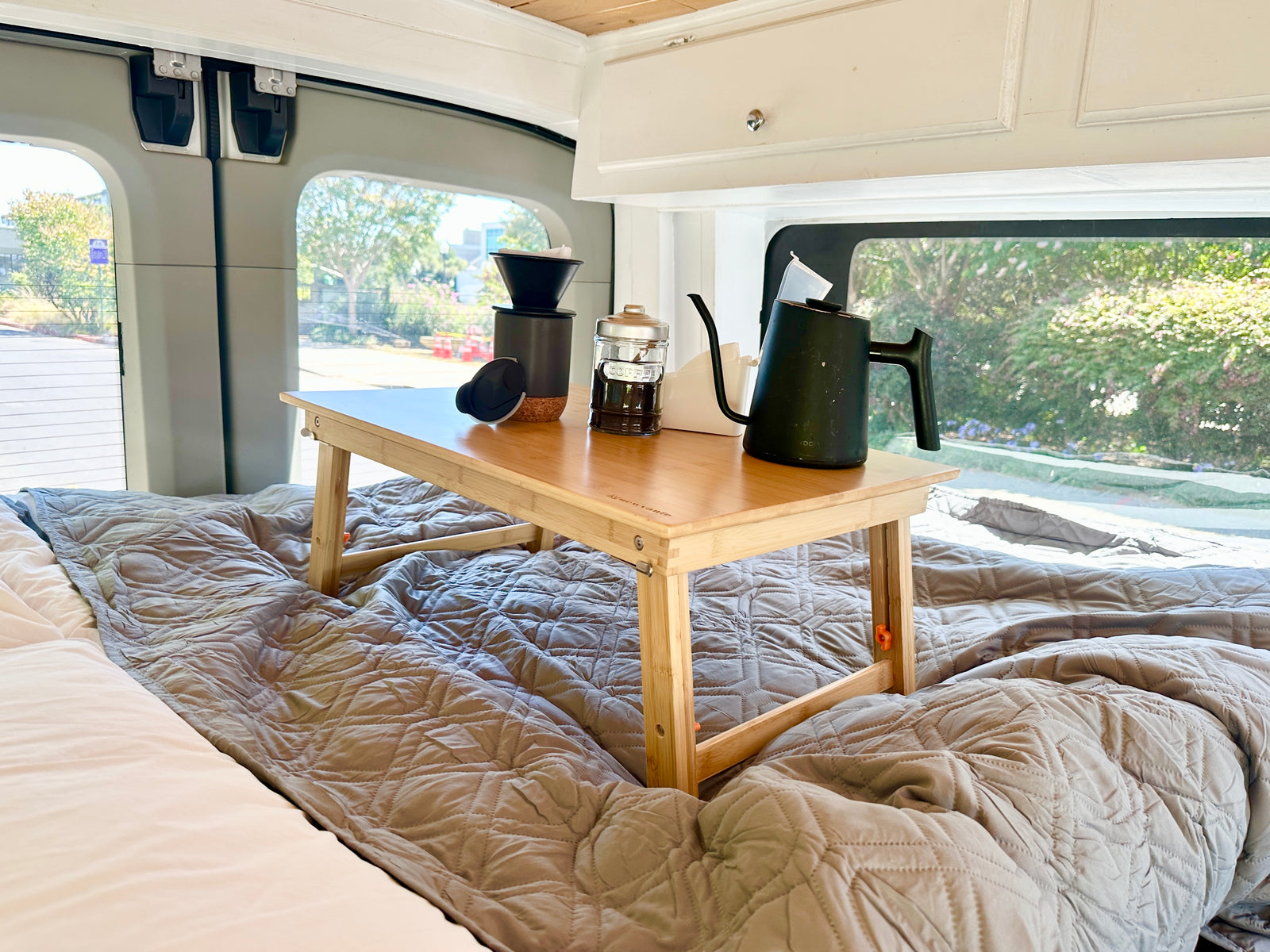 Morning coffee in your RV rental, served on a cozy bed with a wooden tray holding a pour-over kit and kettle.