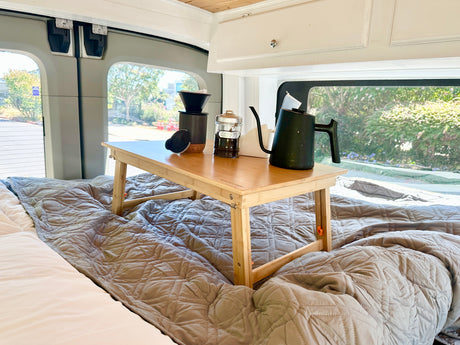 Morning coffee in your RV rental, served on a cozy bed with a wooden tray holding a pour-over kit and kettle.