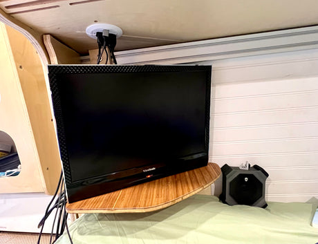 An RV rental's cozy entertainment corner: ViewSonic TV on a wood shelf, cables discreetly routed, beside an Alienware speaker on light green bedding.