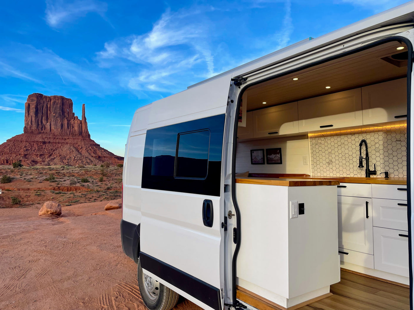 White RV rental with open side door showcasing its modern kitchen, parked in the red desert of Monument Valley.