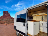 White RV rental with open side door showcasing its modern kitchen, parked in the red desert of Monument Valley.