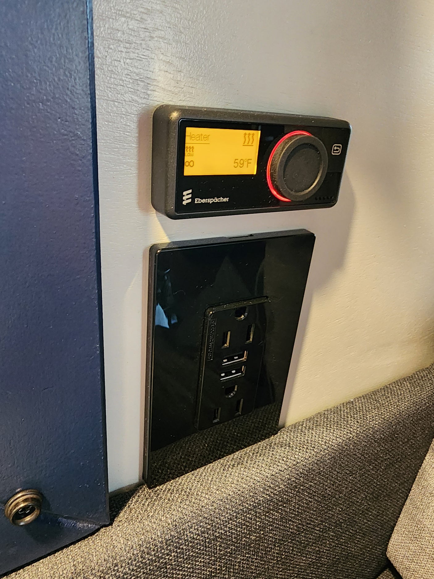 RV rental interior: A black Eberspächer heater control shows 59°F, beside a black power outlet with AC and USB, for climate and charging.