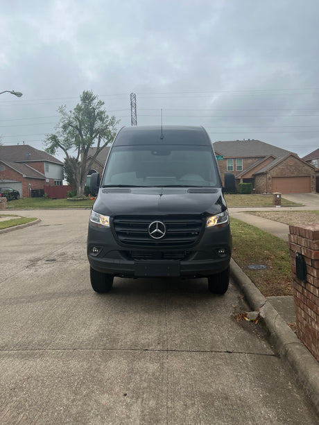 Black Mercedes-Benz Sprinter van, ideal for RV rental, parked on a suburban driveway under a cloudy sky.