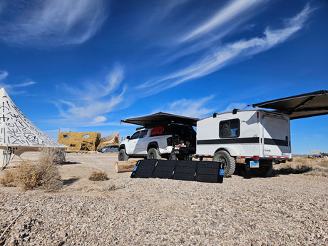 Overland RV rental setup with white pickup truck, camping trailer, and solar panels in a remote desert landscape.