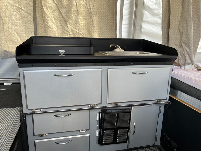 View of a light gray RV rental kitchenette with black counters, sink, faucet, & numerous storage cabinets. — photo 8