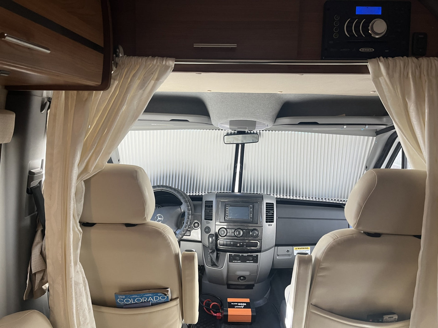 Inside a spacious RV rental. View towards the front cockpit with beige seats, dashboard, and a pulled sunshade.