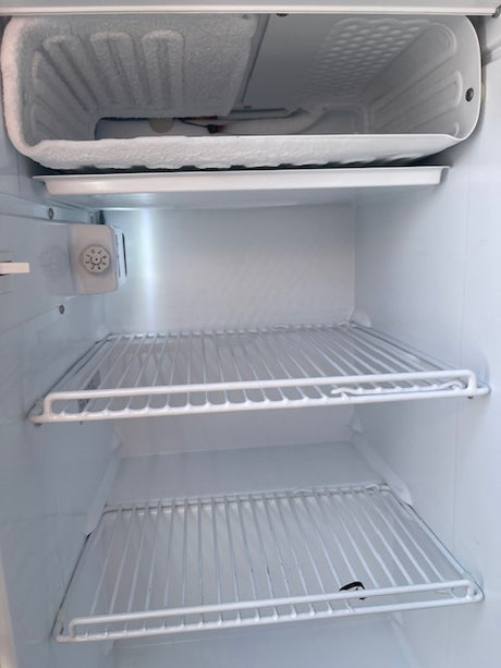 View inside an RV rental's compact refrigerator: frosty evaporator coils, wire shelves & temperature control. Ready for travel food storage!