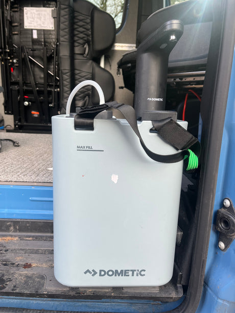 A light gray Dometic portable water container with a black pump inside an RV rental. Great for hydration on trips.