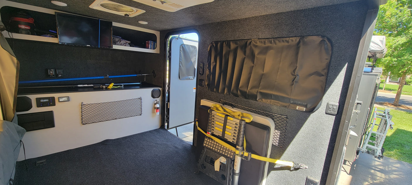 Inside this organized RV rental: dark interior, TV, storage, controls, and a secured folding ladder/table for easy travel.