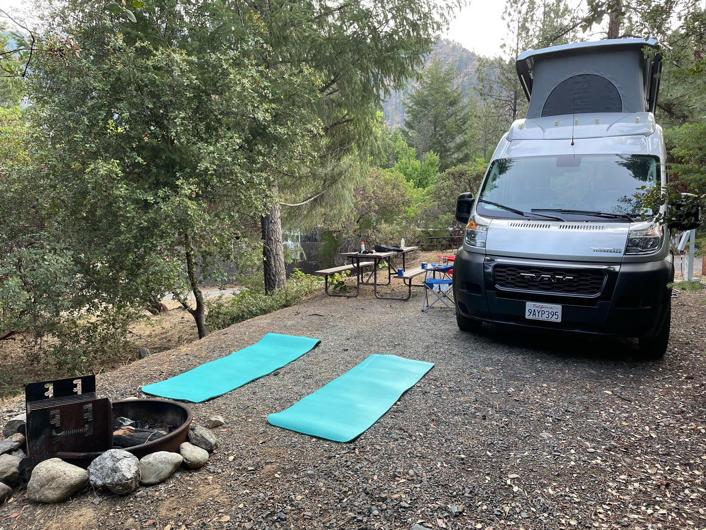 Relax at your rv rental campsite! Silver camper van, yoga mats, and fire pit offer a perfect nature retreat.