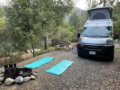 Relax at your rv rental campsite! Silver camper van, yoga mats, and fire pit offer a perfect nature retreat.