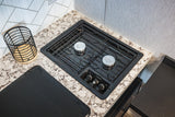 Compact RV rental kitchen with a Dometic two-burner gas stove, speckled countertop, and a light-colored geometric backsplash.