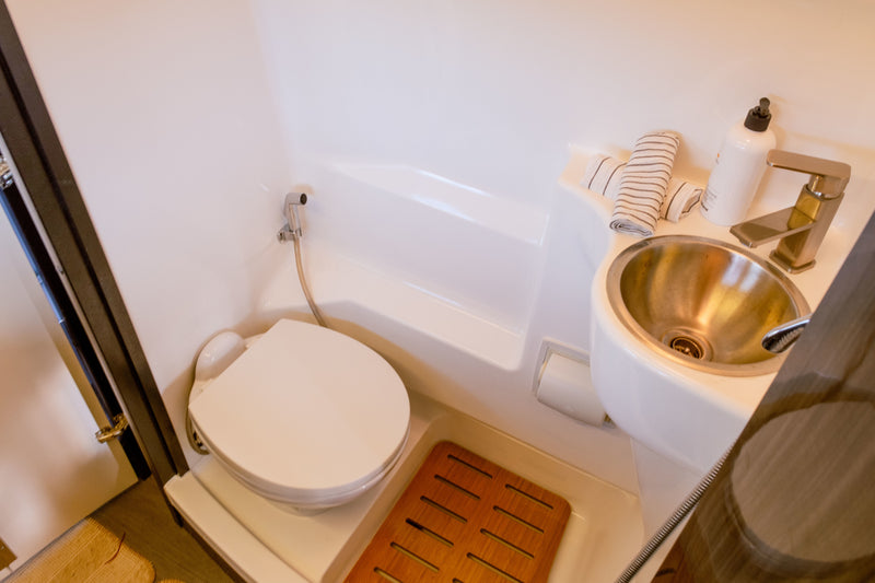 Compact RV rental bathroom: toilet, metal sink, bidet sprayer, and wooden floor mat. — photo 10