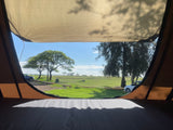 Wake up to stunning views! RV rental tent camping overlooking a sunny coastal park with trees, cars, & ocean.