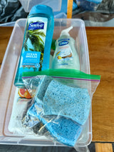 RV rental essentials: body wash, hand soap, and blue sponges neatly organized in a clear bin for travel.