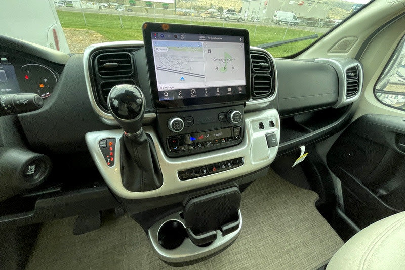RV rental interior: modern driver's area with large touchscreen display, automatic shifter, and climate controls.