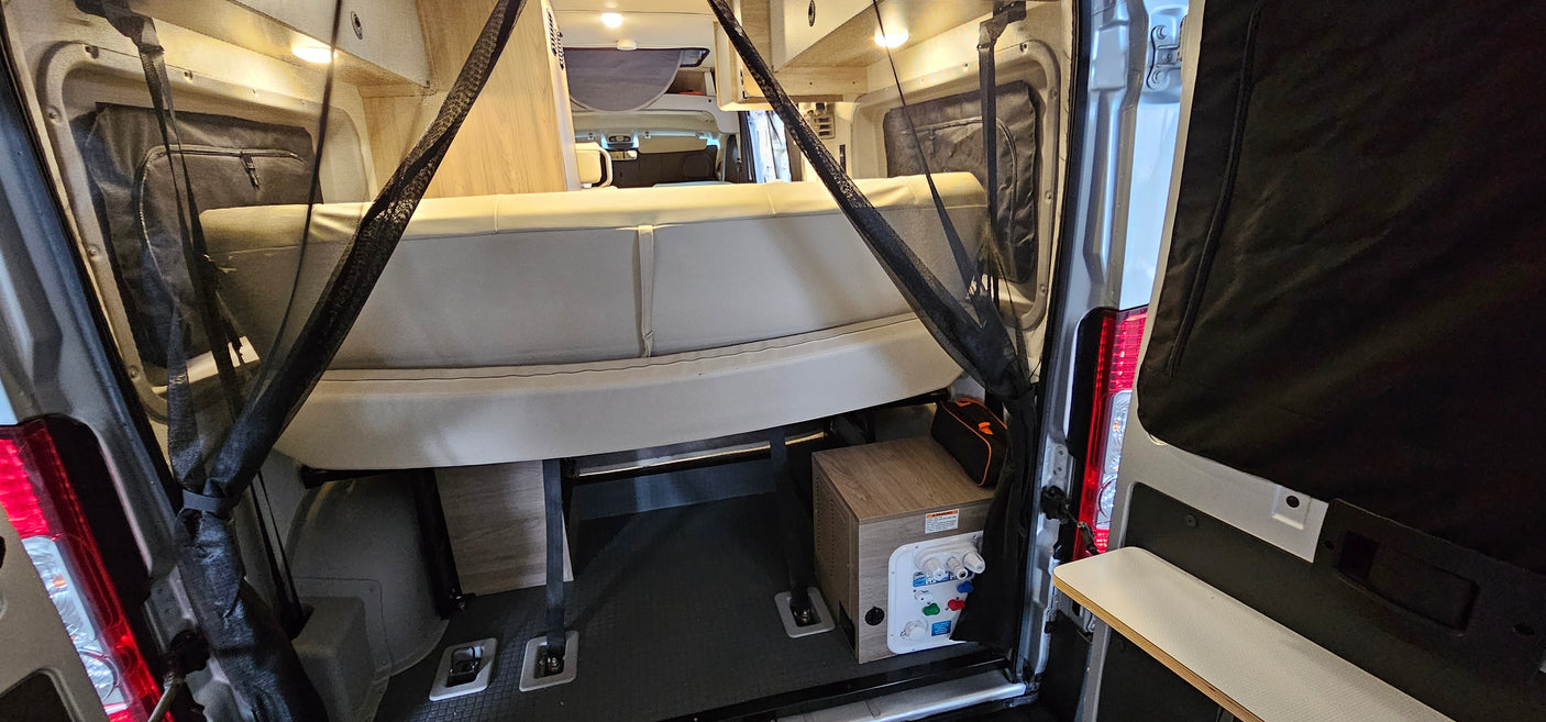 RV rental camper van interior. Features a rear bench seat/bed, utility panel, and protective mesh screens for comfort.